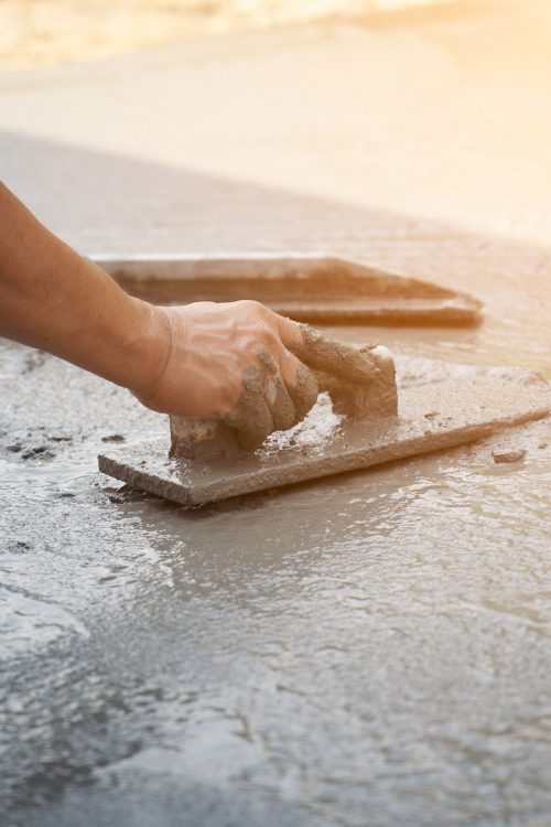 Close up of hands using trowel to scrape excess concrete